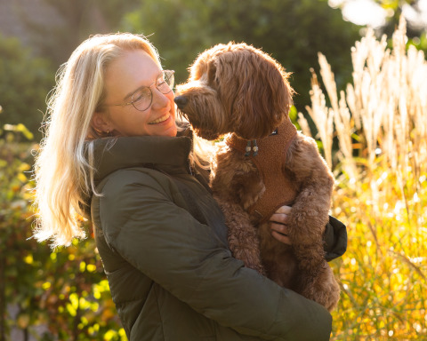 Mujer rubia con gafas sostiene un perro marrón frente a Wellness Lodge XL en Hof van Salland, Países Bajos.