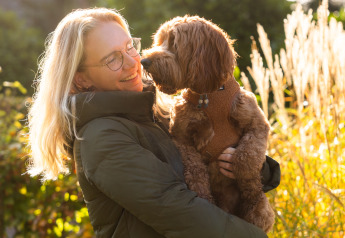 Mujer rubia con gafas sostiene un perro marrón frente a Wellness Lodge XL en Hof van Salland, Países Bajos.