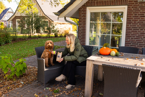 Donna con cane fuori dal Wellness Lodge XL a Hof van Salland, Paesi Bassi, zucche sul tavolo.