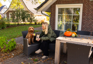 Mujer con perro afuera de Wellness Lodge XL en Hof van Salland, Países Bajos, con calabazas en la mesa.