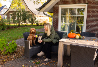 Mujer con perro afuera de Wellness Lodge XL en Hof van Salland, Países Bajos, con calabazas en la mesa.