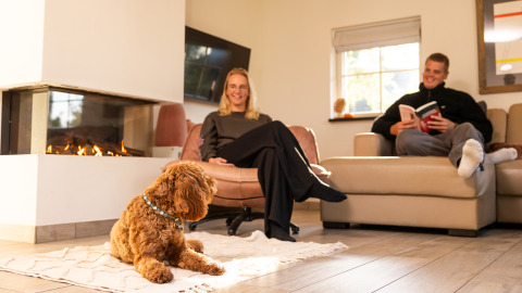 Pareja relajándose con su perro junto a la chimenea en Wellness Lodge XL de Hof van Salland, Países Bajos.