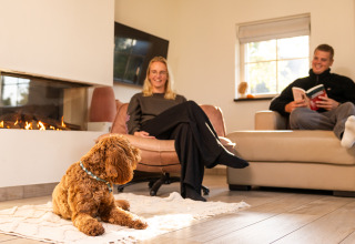 Pareja relajándose con su perro junto a la chimenea en Wellness Lodge XL de Hof van Salland, Países Bajos.