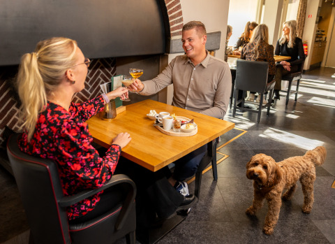 Pareja disfruta postre y bebidas con su perro en Wellness Lodge XL, Hof van Salland, Países Bajos.