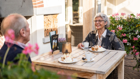 Pareja mayor disfruta café y pastel al aire libre en Wellness Lodge XL en Hof van Salland, Países Bajos.