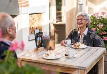Pareja mayor disfruta café y pastel al aire libre en Wellness Lodge XL en Hof van Salland, Países Bajos.