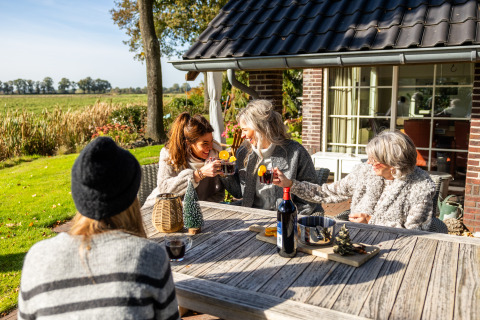 Cuatro mujeres disfrutan de bebidas en la terraza de la Wellness Lodge XL, tiny house en Hof van Salland, Países Bajos.