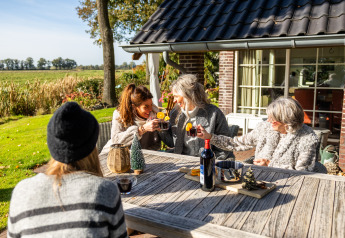 Cuatro mujeres disfrutan de bebidas en la terraza de la Wellness Lodge XL, tiny house en Hof van Salland, Países Bajos.