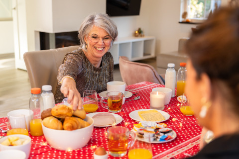 Mujer sonríe en desayuno con jugo y bollería en Wellness Lodge XL en Hof van Salland, Países Bajos.