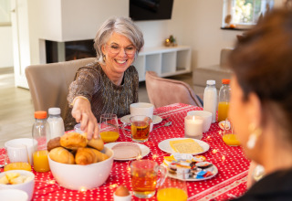 Woman smiling at breakfast table with juice and pastries in Wellness Lodge XL at Hof van Salland, Netherlands.