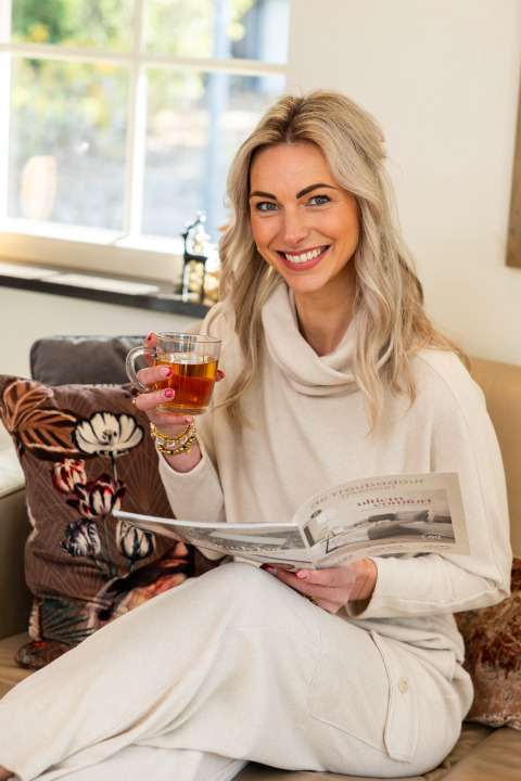 Mujer disfrutando una taza de té y leyendo una revista en Wellness Lodge XL de Hof van Salland, Países Bajos.