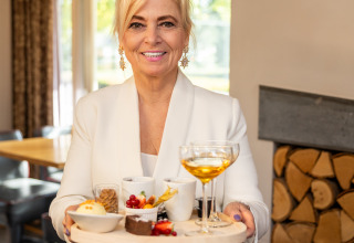 Mujer con chaqueta blanca sirviendo postres y bebida en Wellness Lodge XL, Hof van Salland, Países Bajos.