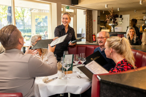 Un grupo pide comida a una camarera sonriente en un restaurante acogedor, sentados con las cartas del menú.