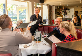 Een groep bestelt bij een lachende serveerster in een knus restaurant, met menukaarten in de hand.