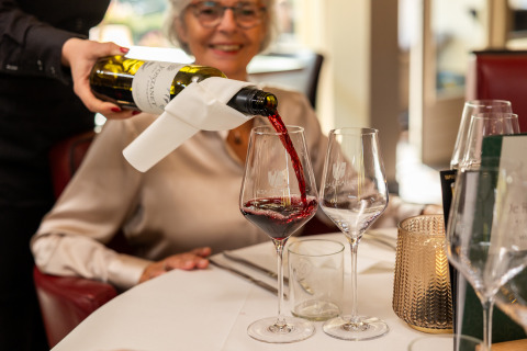 Un camarero sirve vino tinto en una copa para una mujer sonriente en Wellness Lodge XL en Hof van Salland.