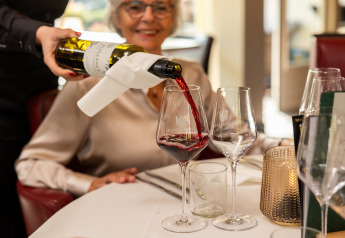 Un camarero sirve vino tinto en una copa para una mujer sonriente en Wellness Lodge XL en Hof van Salland.