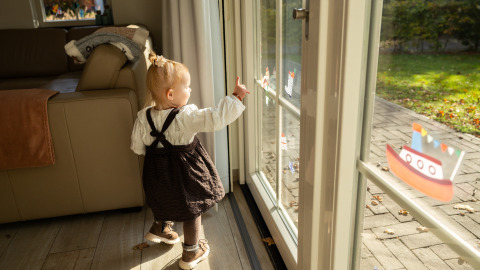 Toddler looks outside through glass doors at Wellness Lodge XL, Hof van Salland, Netherlands, with boat stickers.