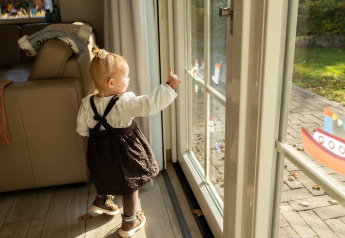Petit enfant regarde dehors par la porte vitrée à Wellness Lodge XL, Hof van Salland, Pays-Bas, avec autocollants de bateau.
