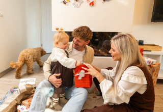 Familia abre regalos en la Wellness Lodge XL de Hof van Salland, Países Bajos, con su perro cerca.