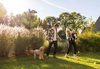 Familia con niño y perro disfruta del sol frente a la Wellness Lodge XL en Hof van Salland, Países Bajos.