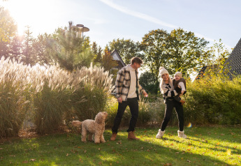 Familia con niño y perro disfruta del sol frente a la Wellness Lodge XL en Hof van Salland, Países Bajos.