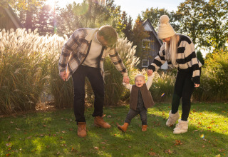 Familia caminando de la mano en el jardín de Wellness Lodge XL, Hof van Salland, Países Bajos, en un día soleado.