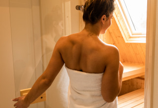 Mujer con toalla blanca entra en la sauna en Wellness Lodge XL, Hof van Salland, Países Bajos.