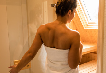 Woman in white towel enters sauna at Wellness Lodge XL, Hof van Salland, Netherlands.
