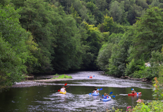 People kayaking on a scenic river bordered by lush woods at a glamping accommodation in the wilderness.