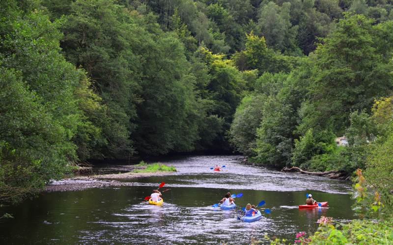 Persone fanno kayak su un fiume immerso nel verde, vicino a una struttura di glamping nella natura.
