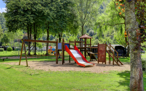 Speeltuin met glijbaan en schommels bij een glampingverblijf, omgeven door bomen en natuur.