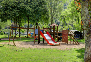 Speeltuin met glijbaan en schommels bij een glampingverblijf, omgeven door bomen en natuur.