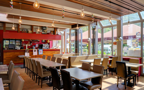 Bright, modern café area at a glamping resort featuring large windows, ample seating, and a bar.