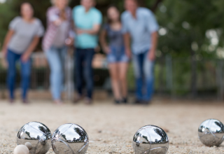 Vier mensen spelen petanque bij een glampingverblijf, met glimmende ballen scherp op de voorgrond.
