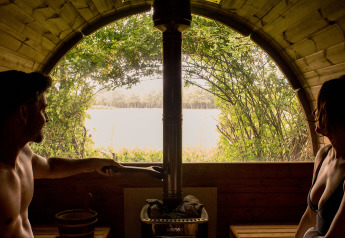 Pareja relajándose en una sauna acogedora con vista al lago desde un alojamiento de glamping en la naturaleza.
