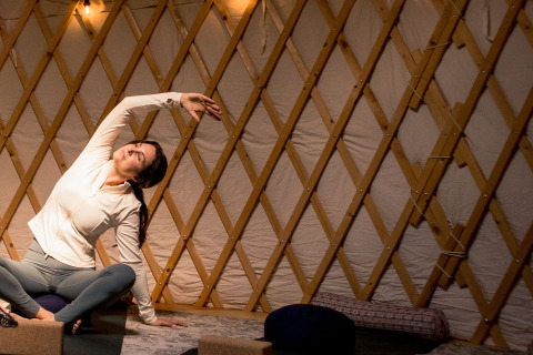 Mujer practicando yoga en una yurta con estructura de madera y luz suave, ambiente de glamping.