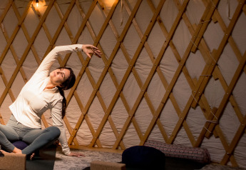 Vrouw doet yoga in een houten yurt met zachte verlichting, sfeer van luxe kamperen (glamping).