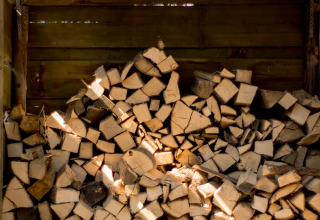 Stak træbrænde opbevaret i et træshelter, klar til brug på en hyggelig glampingoplevelse i naturen.