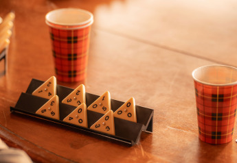 Tavolo con bicchieri di carta scozzesi e tessere da gioco triangolari in un alloggio glamping accogliente.