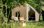 Moderne tiny house Luxe & Lazy Lodge gemt blandt frodige træer hos RØSTIG Dorst, Holland, med hyggelig udendørs siddeplads.