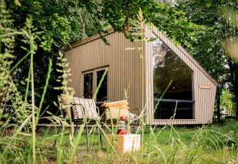 Moderne tiny house Luxe & Lazy Lodge gemt blandt frodige træer hos RØSTIG Dorst, Holland, med hyggelig udendørs siddeplads.