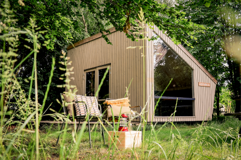 Moderne tiny house Luxe & Lazy Lodge gemt blandt frodige træer hos RØSTIG Dorst, Holland, med hyggelig udendørs siddeplads.