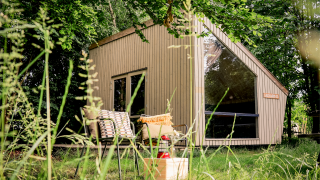 Moderne tiny house Luxe & Lazy Lodge gemt blandt frodige træer hos RØSTIG Dorst, Holland, med hyggelig udendørs siddeplads.