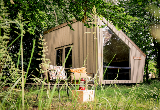 Moderne tiny house Luxe & Lazy Lodge gemt blandt frodige træer hos RØSTIG Dorst, Holland, med hyggelig udendørs siddeplads.