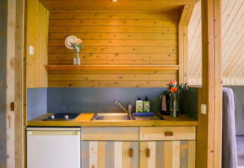 Lille køkken med træpaneler, vask, kogeplader, køleskab og blomster i glasvaser i Luxe & Lazy Lodge.