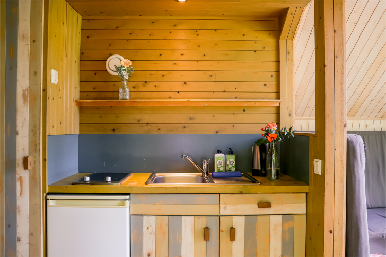 Pequeña cocina de madera con fregadero, placa, nevera y flores en jarrones en Luxe & Lazy Lodge.