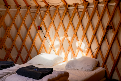 Innenraum einer gemütlichen Jurte mit Doppelbett und Holzgitter bei RØSTIG Dorst in den Niederlanden.