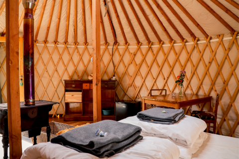 Interieur van de yurt bij RØSTIG Dorst in Nederland met bedden, tafel, houtkachel en houten meubels.