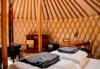 Interieur van de yurt bij RØSTIG Dorst in Nederland met bedden, tafel, houtkachel en houten meubels.