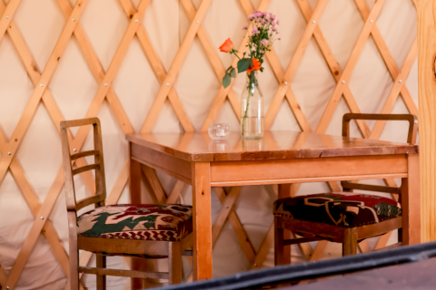 Mesa de madera con dos sillas y un jarrón de flores dentro de una yurta en Yurt at RØSTIG Dorst, Países Bajos.